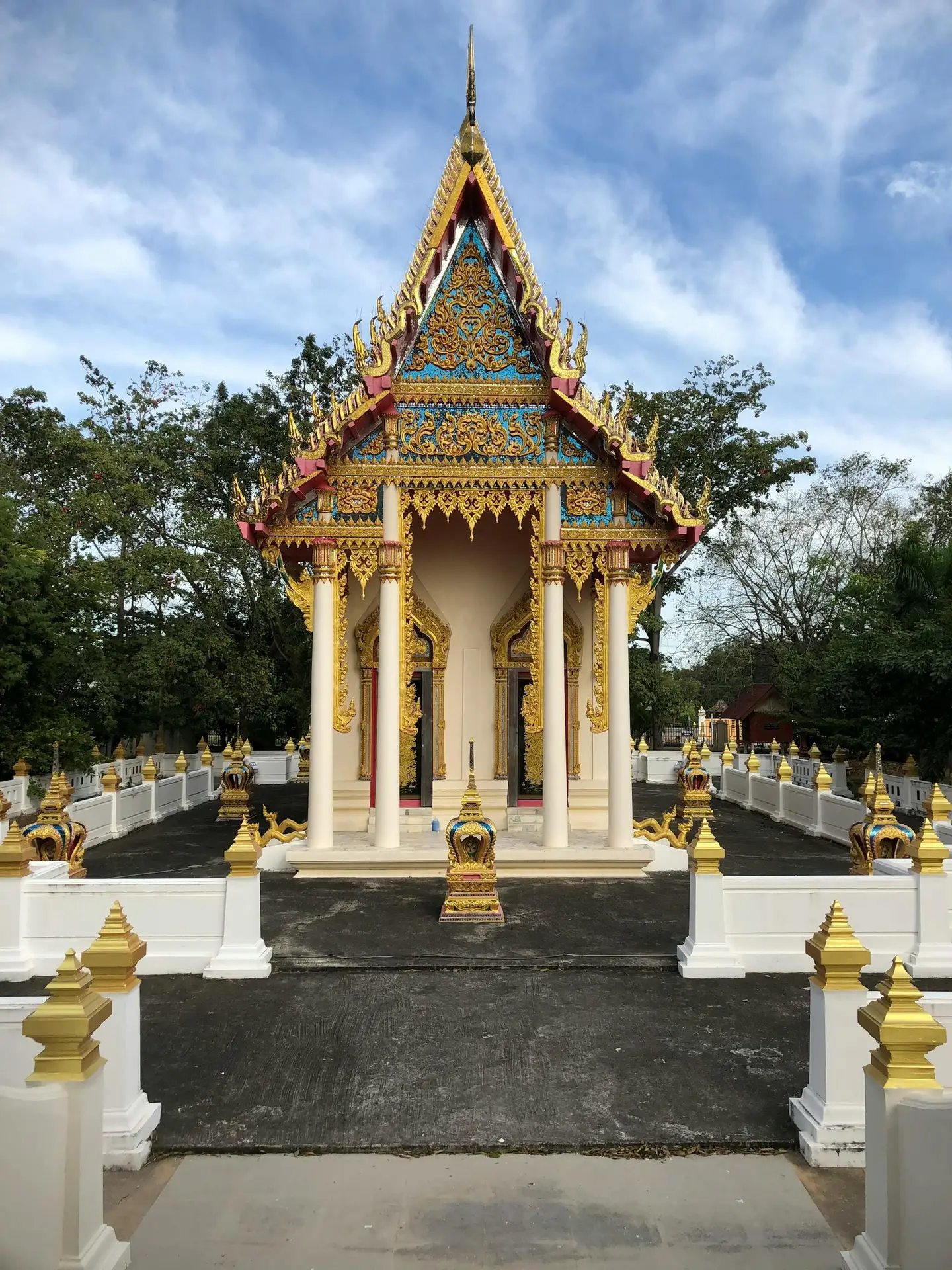 A beautiful ornate Thai Buddhist temple with gold and turquoise details surrounded by trees